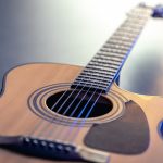 Acoustic guitar, music instrument resting against a dark black background.